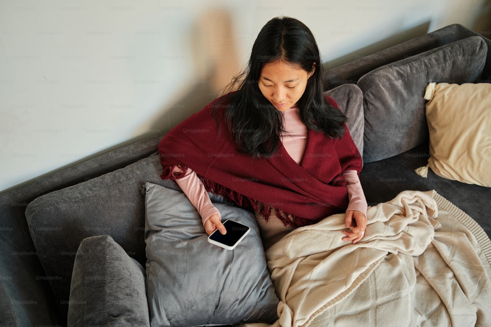 eine Frau sitzt auf einer Couch und hält ein Handy in der Hand