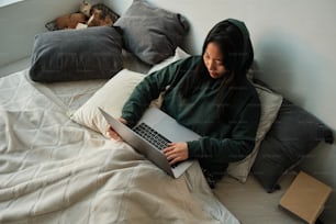 ベッドに座った女性がノートパソコンを使う