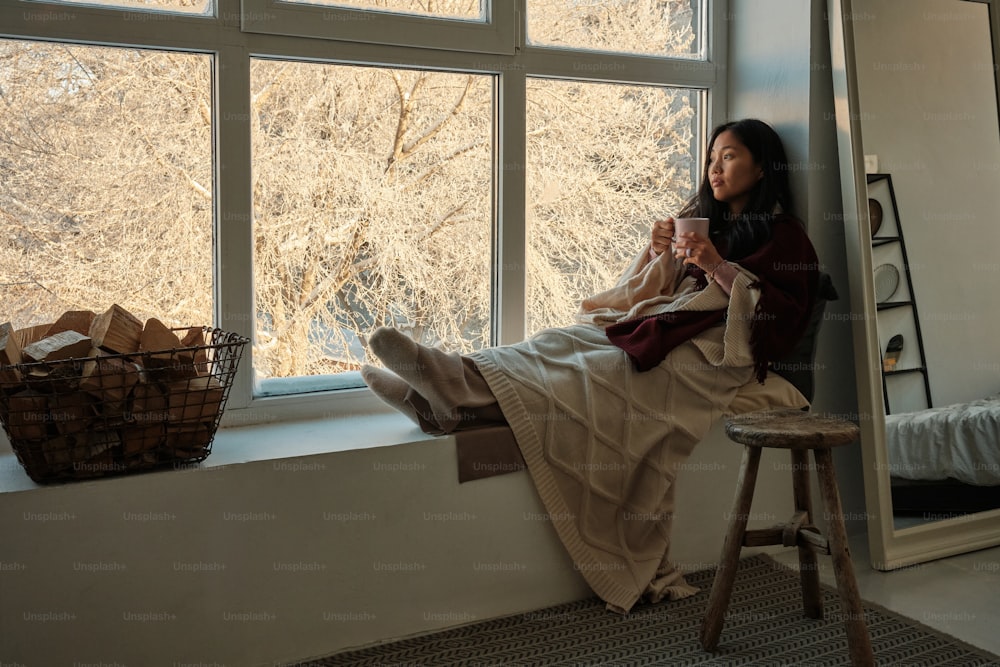 eine Frau, die auf einem Fensterbrett sitzt und eine Tasse hält