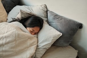 a woman sleeping in a bed with a blanket and pillows