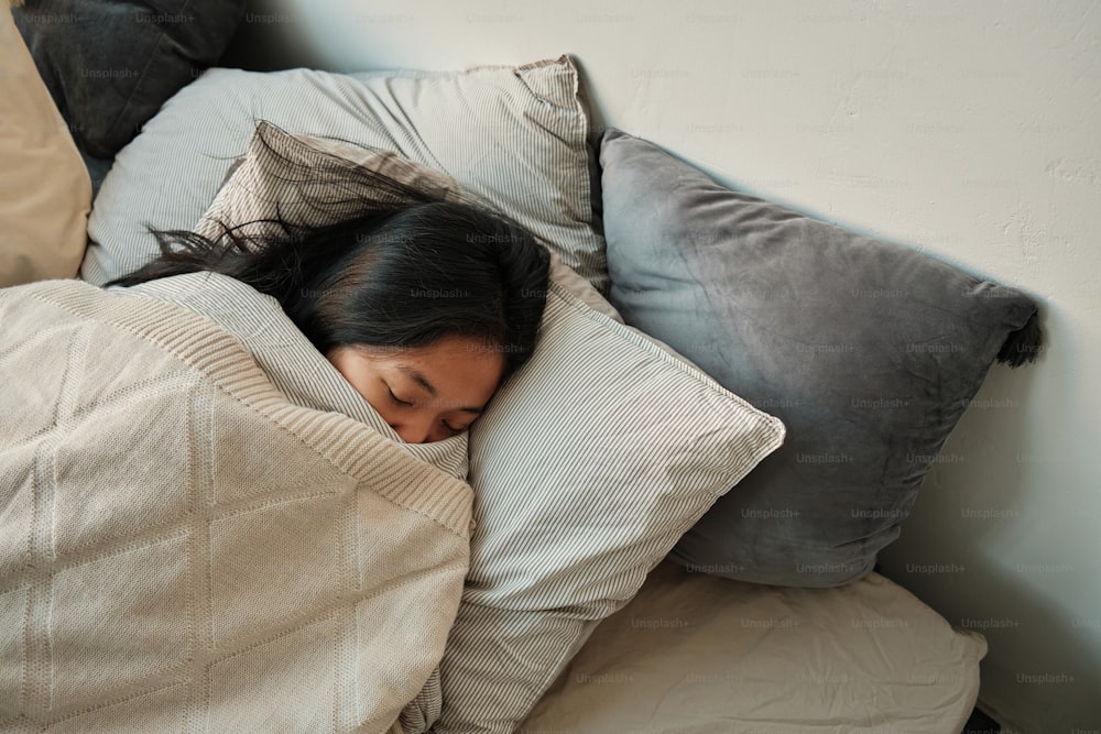 a woman sleeping in a bed with a blanket and pillows