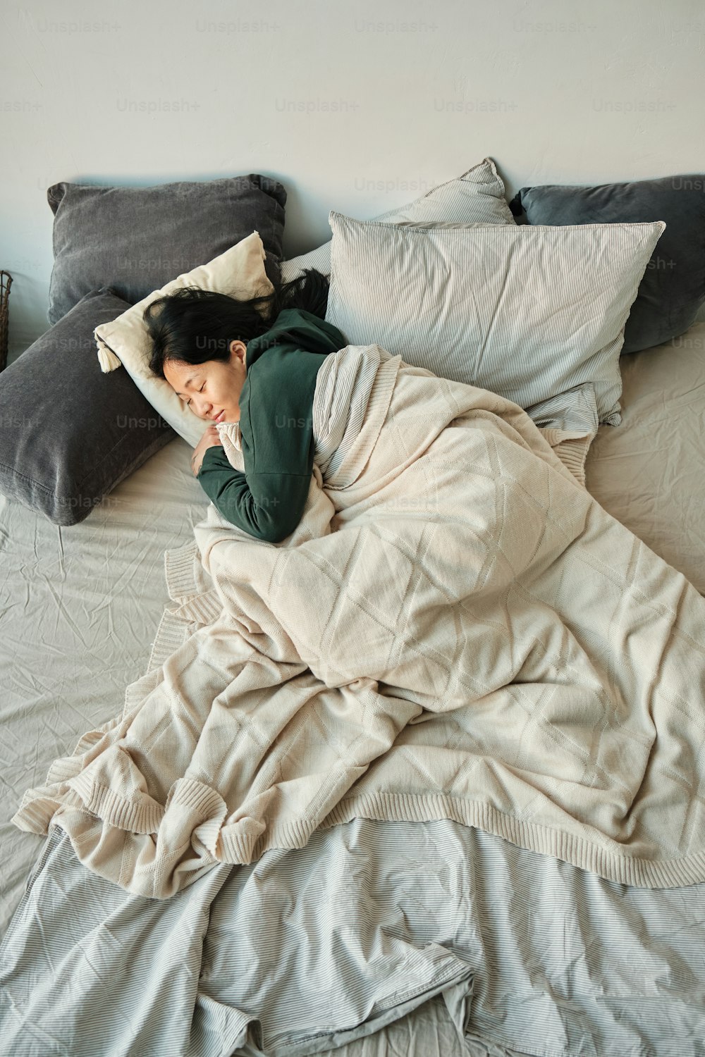 枕がたくさん敷き詰められたベッドで女性が寝ている