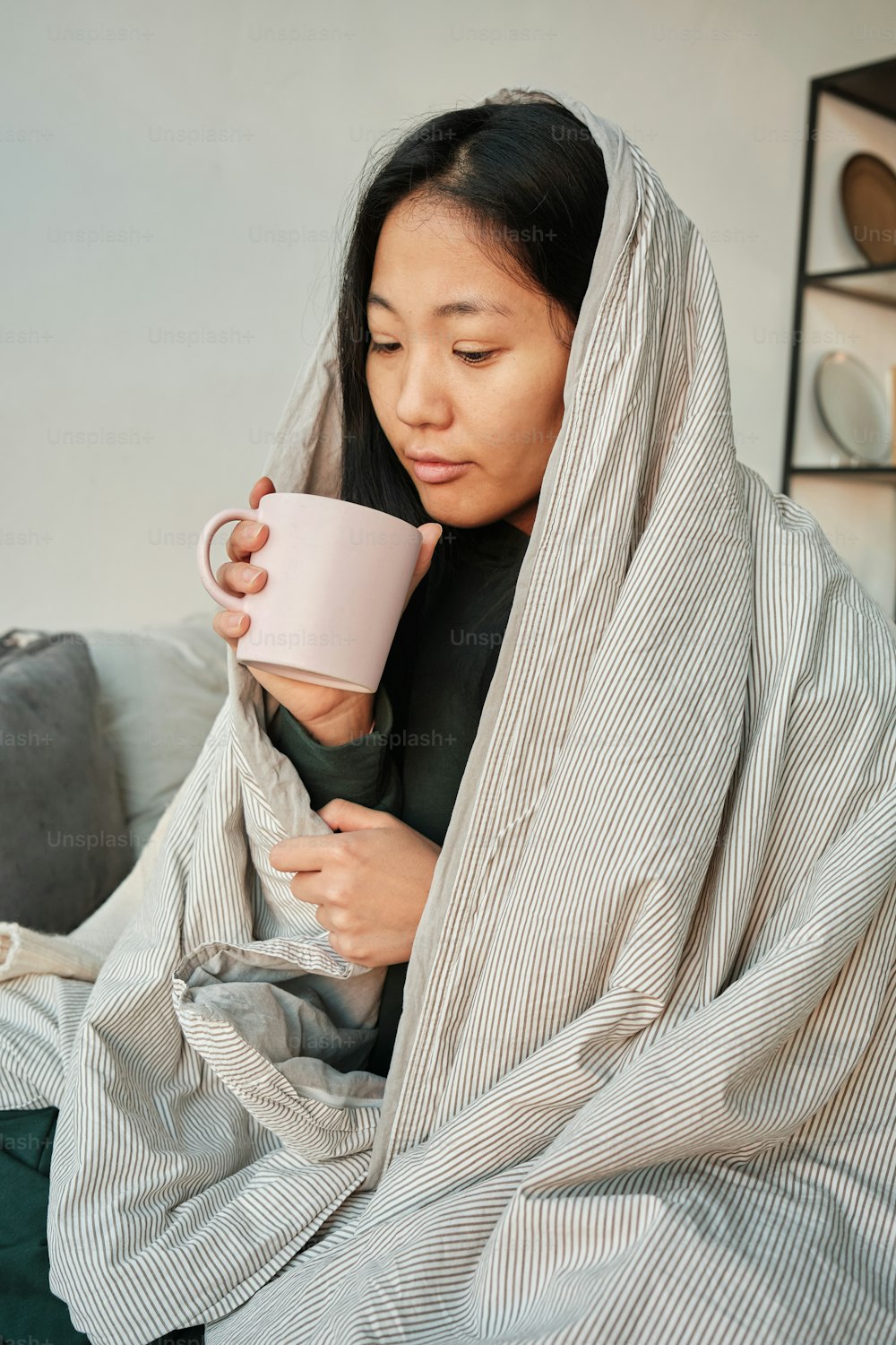 una donna avvolta in una coperta che regge una tazza