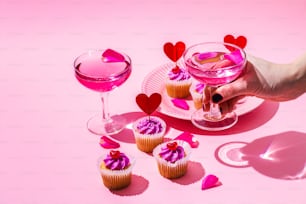 uma mesa rosa coberta com cupcakes e uma taça de vinho