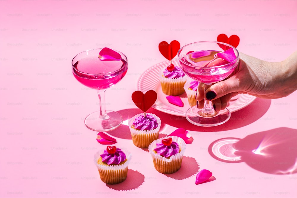 a pink table topped with cupcakes and a wine glass
