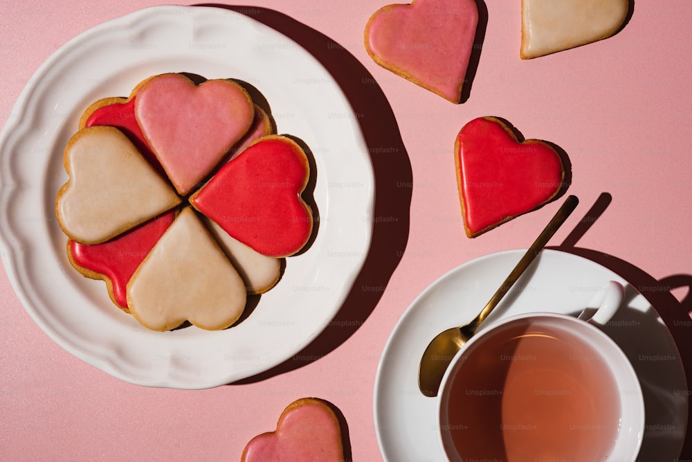 a plate of heart shaped cookies next to a cup of tea