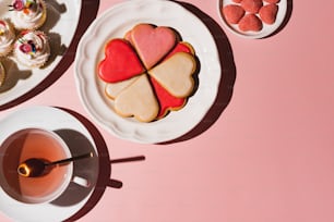 a plate of heart shaped cookies next to a cup of tea