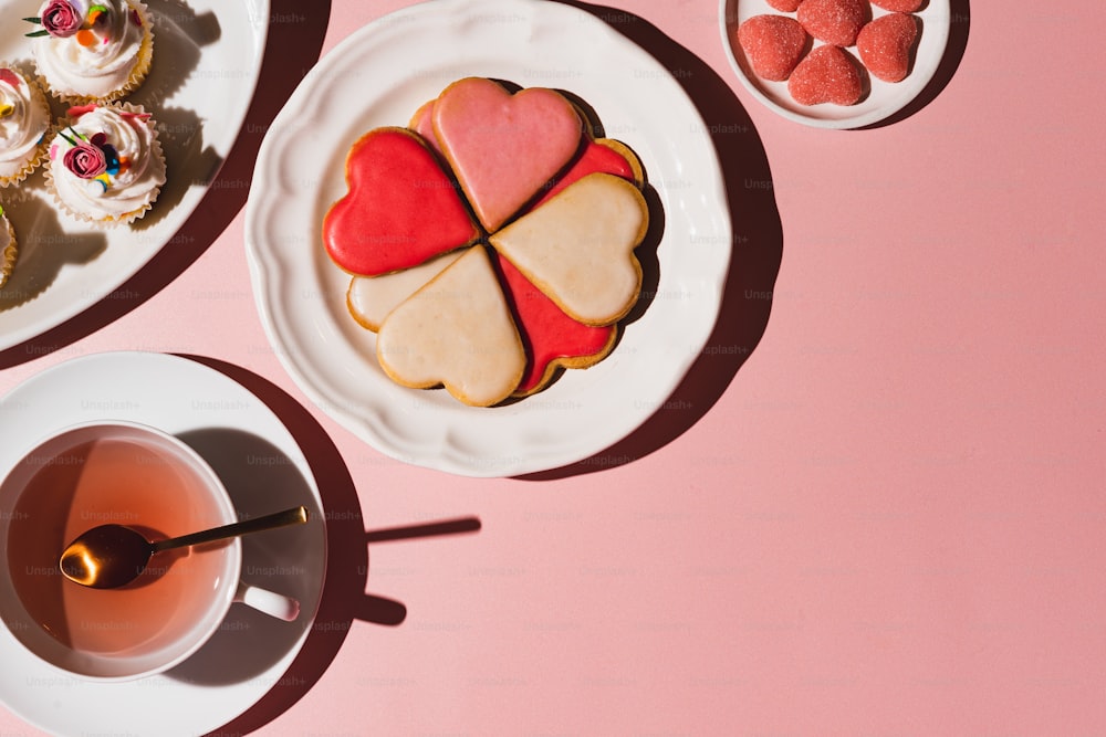 a plate of heart shaped cookies next to a cup of tea