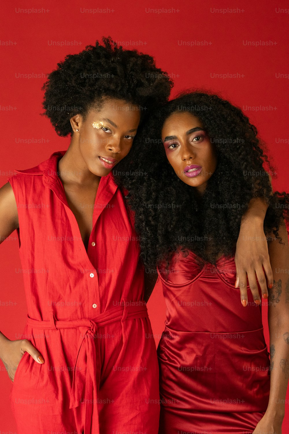 two women standing next to each other in front of a red background