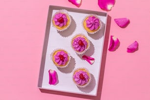 a box of cupcakes with pink frosting on a pink background