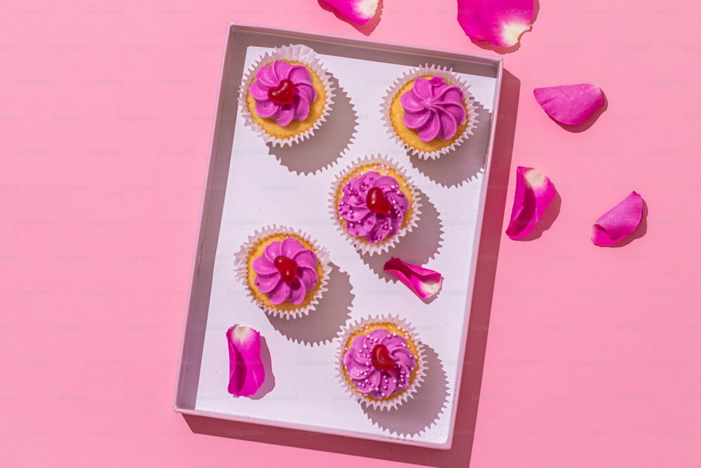 une boîte de cupcakes avec glaçage rose sur fond rose
