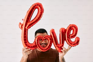 a man holding up two red balloons in the shape of the word love