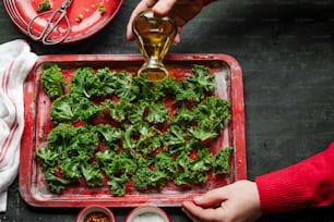 a person pouring olive oil onto a tray of kale