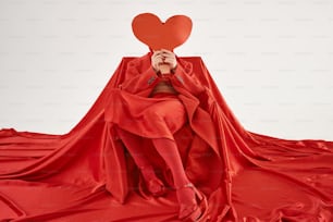 uma mulher em um vestido vermelho segurando um coração vermelho sobre seu rosto