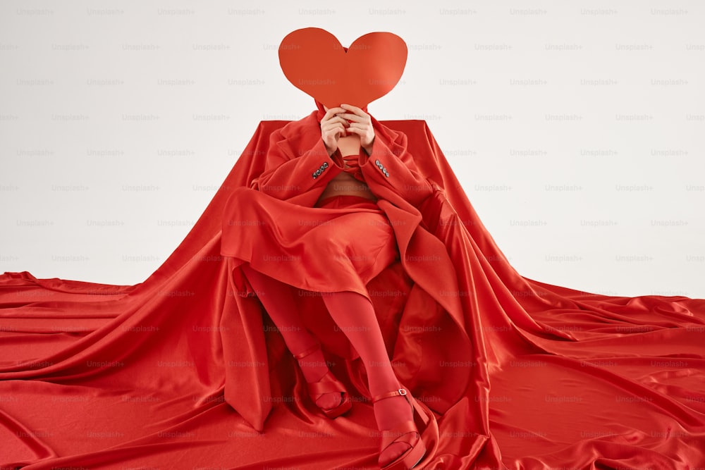 a woman in a red dress holding a red heart over her face