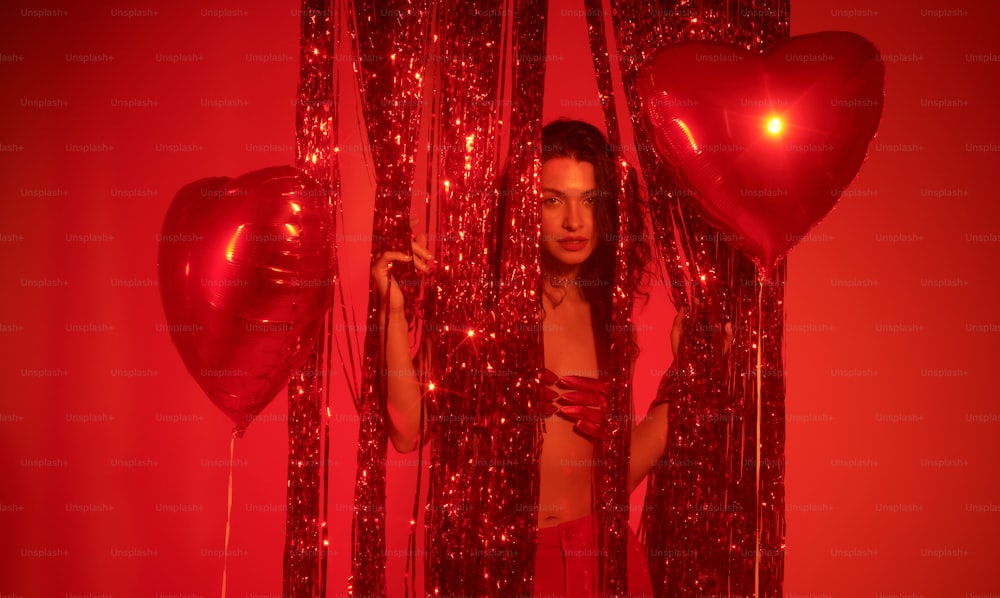 a woman standing behind a curtain with red balloons