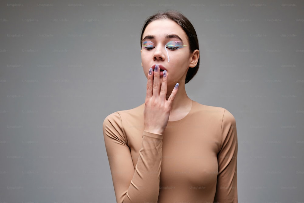 a woman with makeup on her face holding her hands to her mouth