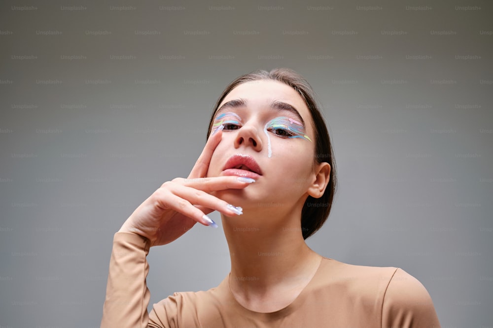 a woman with blue and white makeup holding her hand to her face