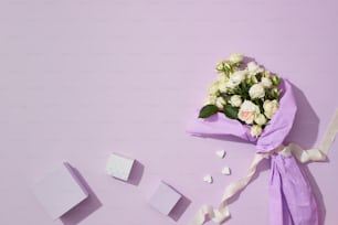 ein Strauß weißer Rosen und eine Geschenkbox auf lila Hintergrund