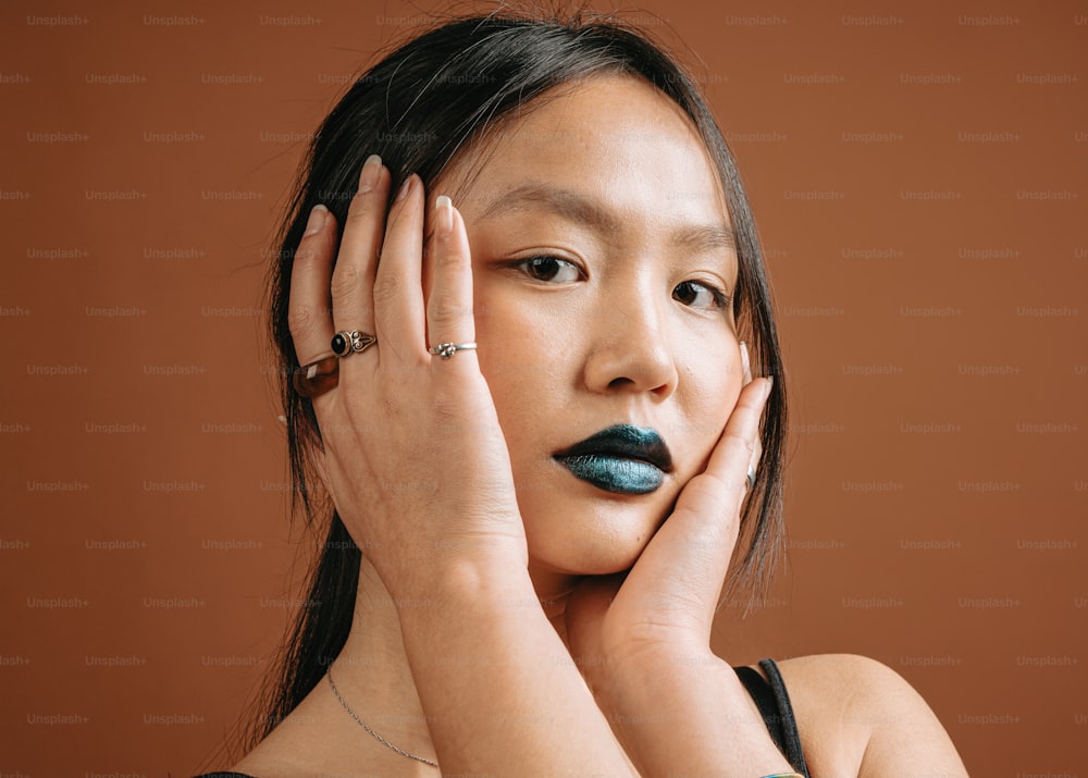 a woman with dark blue lipstick holding her hands to her face