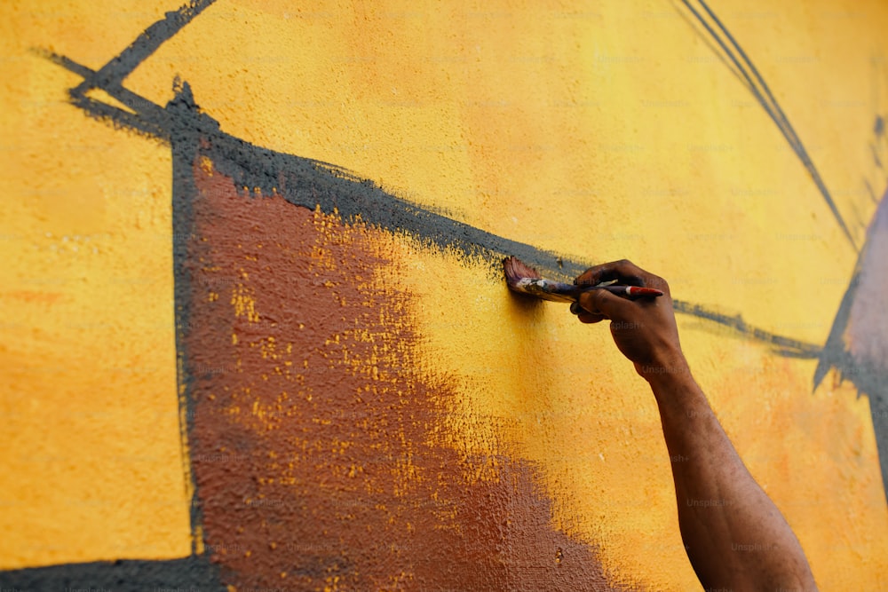 a person painting a wall with yellow and brown paint
