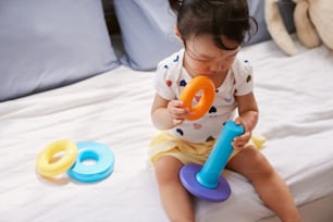 une petite fille assise sur un lit jouant avec un jouet