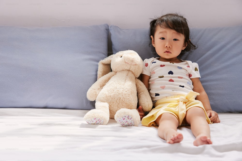 a little girl sitting on a bed with a stuffed animal