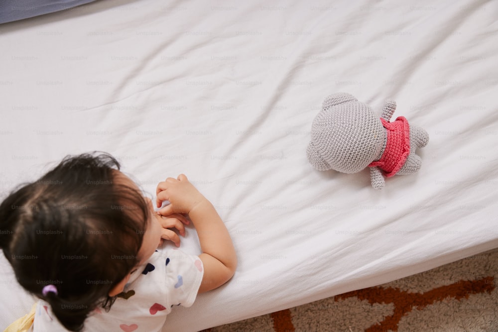 a little girl laying on top of a bed next to a stuffed animal
