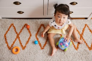 a little girl sitting on the floor playing with a ball