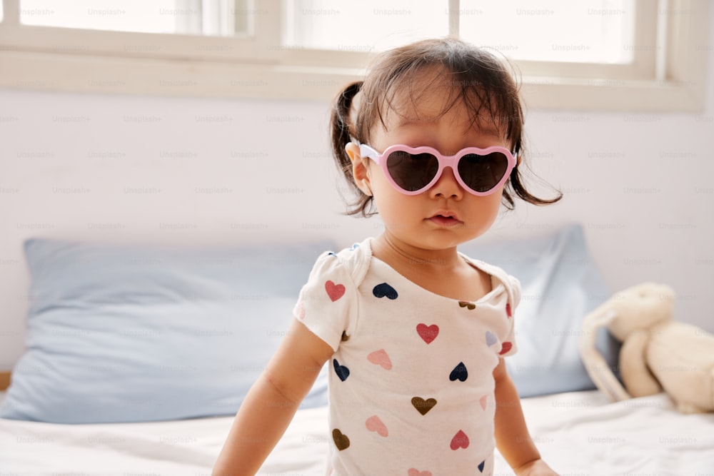 a little girl wearing heart shaped sunglasses on top of a bed