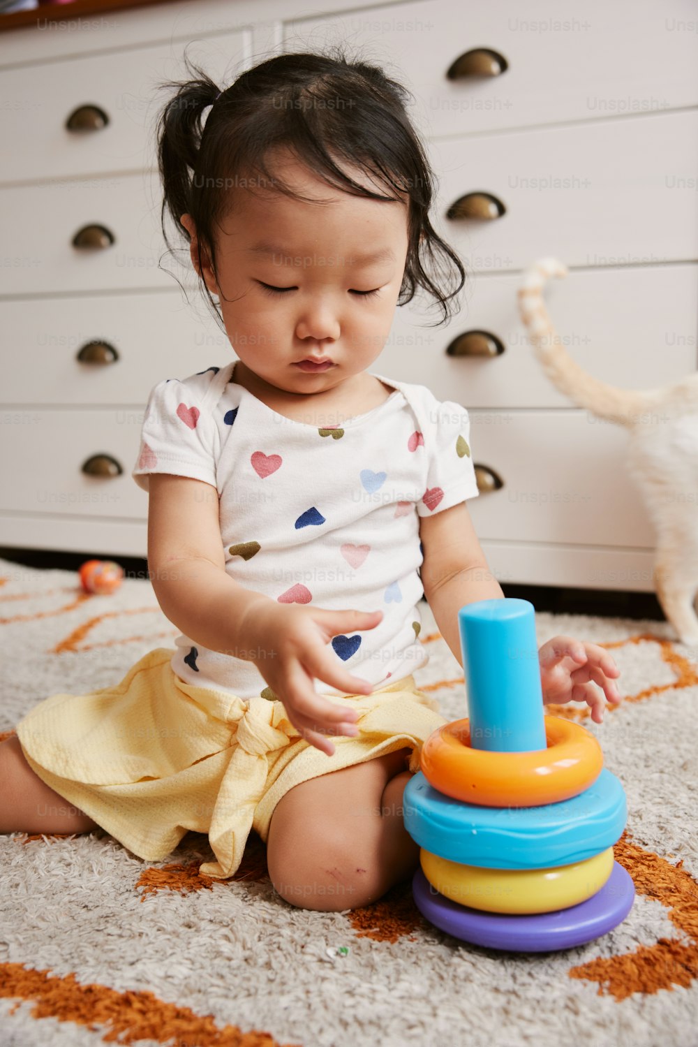 a little girl sitting on the floor playing with a toy