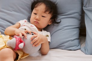 a little girl laying on a bed holding a stuffed animal