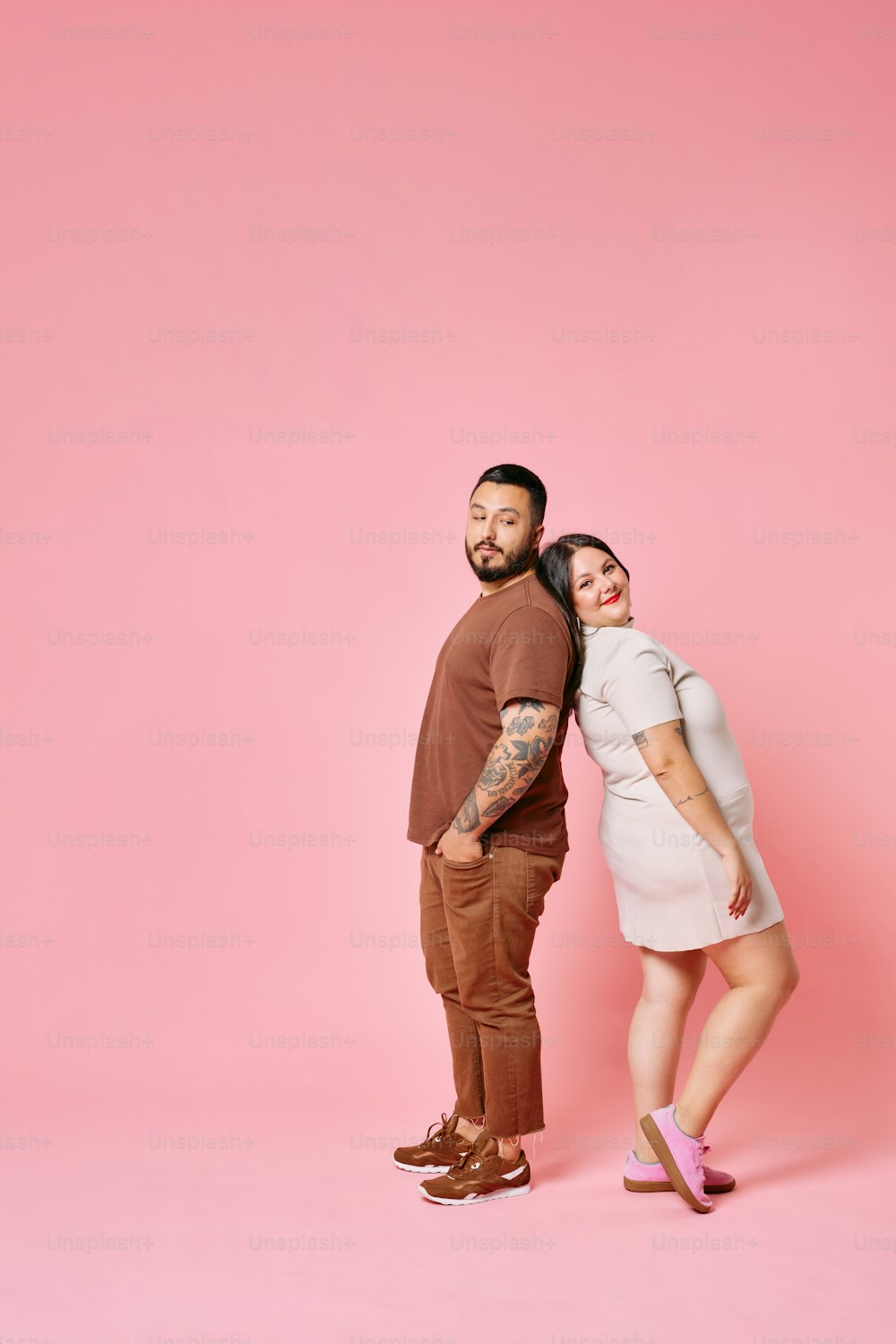 a man and a woman standing in front of a pink background