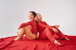 a man and a woman sitting on a red sheet