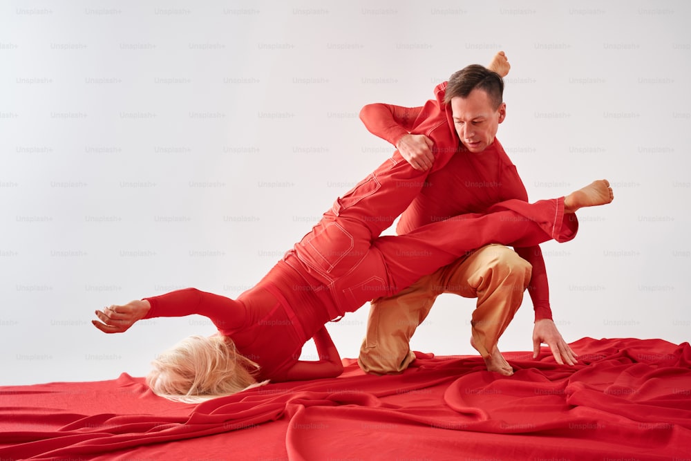 um homem de terno vermelho está fazendo um handstand em uma mulher loira