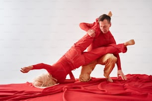 Un hombre con un traje rojo está haciendo una parada de manos sobre una mujer rubia