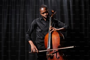 a man holding a cello while standing in front of a curtain