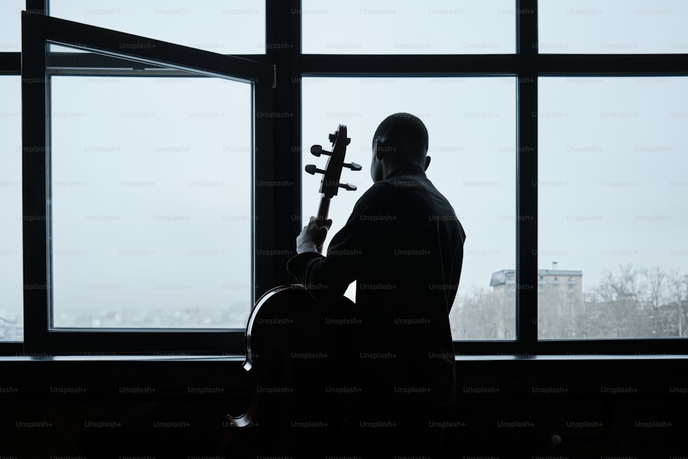 a man holding a violin in front of a window