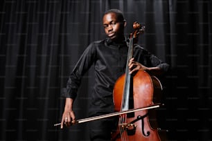 Um homem de camisa preta está segurando um violoncelo
