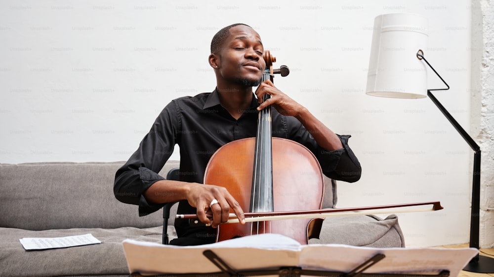 Un hombre sentado en un sofá tocando un violonchelo