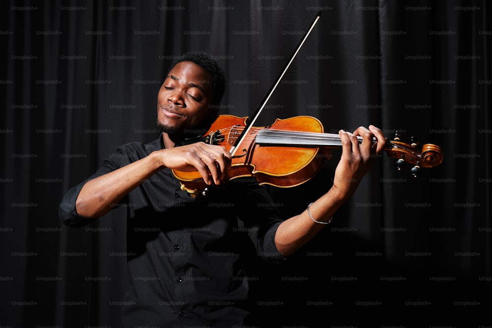 a man playing a violin in front of a black background