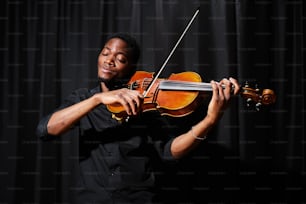 un hombre tocando un violín frente a un fondo negro