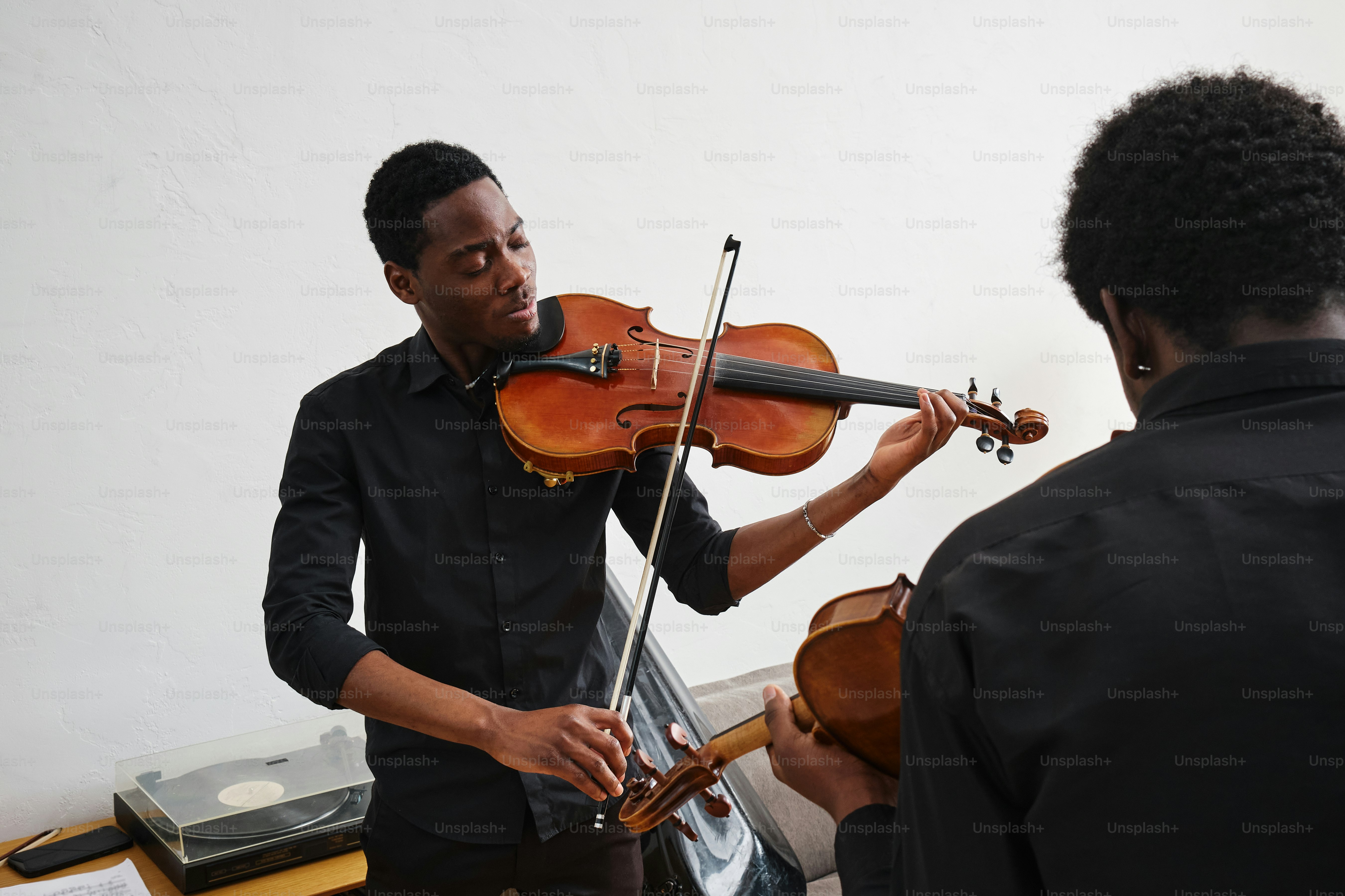A man playing a violin while another man watches photo – Music Image on ...