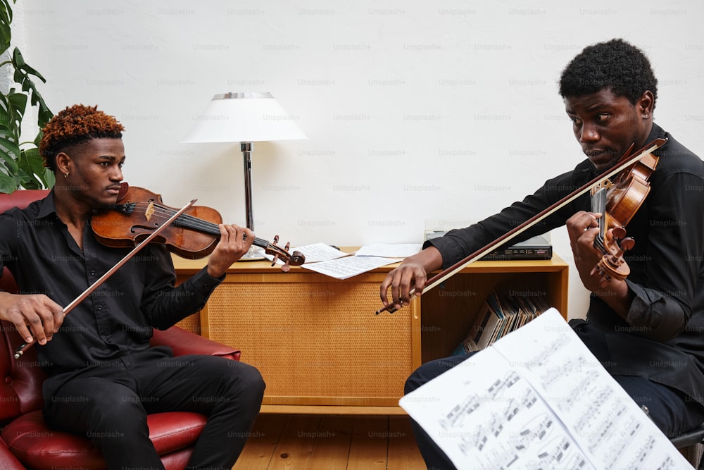 un couple d’hommes assis l’un à côté de l’autre jouant du violon