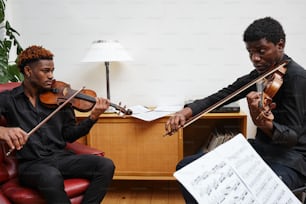 a couple of men sitting next to each other playing violin
