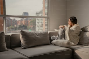 una mujer sentada en un sofá mirando por una ventana