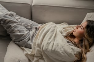 a woman laying on a couch covered in a blanket