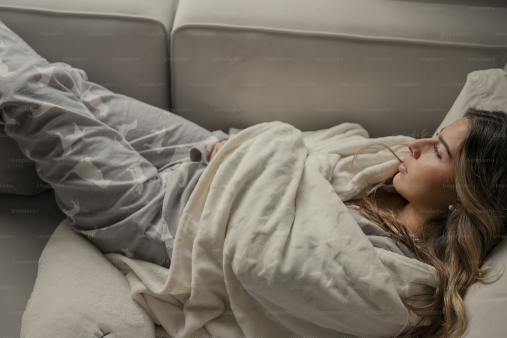 a woman laying on a couch covered in a blanket