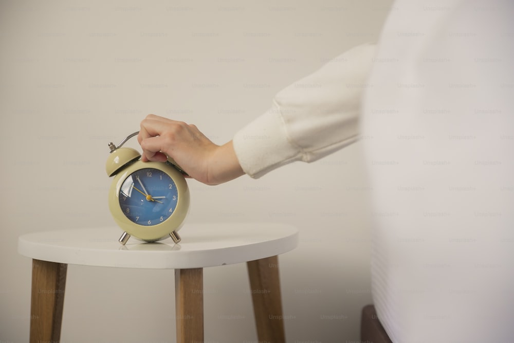 a person holding an alarm clock on a small table