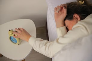a woman laying in bed with a alarm clock on a table